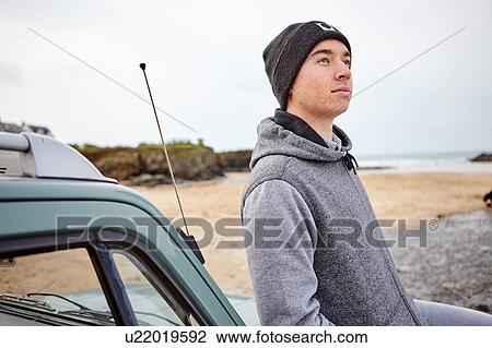 Young man leaning against car gazing upward at beach, Constantine Bay, Cornwall, UK View Large Photo Image Stock Image - Young man leaning against car gazing upward at beach, Constantine Bay, Cornwall, UK. Fotosearch