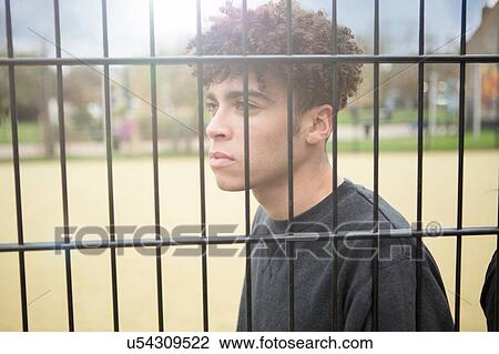 Stock Image - Young man leaning against fence. Fotosearch