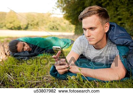 Young man lying sleeping bag texting on smartphone in field View Large Photo Image Stock Image - Young man lying sleeping bag texting on smartphone in field. Fotosearch