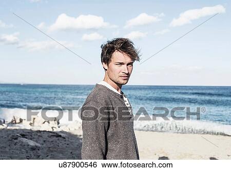 Young man on beach in front of ocean looking at camera, Costa Smeralda, Sardinia, Italy View Large Photo Image Stock Photograph - Young man on beach in front of ocean looking at camera, Costa Smeralda, Sardinia, Italy. Fotosearch