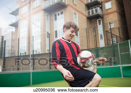 Stock Photograph - Young man practising football skills on urban football pitch. Fotosearch