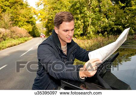 Young man reading map on rural road View Large Photo Image Stock Photo - Young man reading map on rural road. Fotosearch