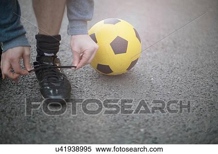 Young man tying shoelaces, football beside him, low section View Large Photo Image Stock Photography - Young man tying shoelaces, football beside him, low section. Fotosearch