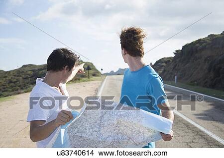 Picture - Young men on road holding map, looking over shoulder pointing, Costa Smeralda, Sardinia, Italy. Fotosearch