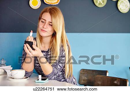 Young woman alone in cafe applying lipstick View Large Photo Image Stock Image - Young woman alone in cafe applying lipstick. Fotosearch