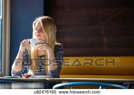 Stock Photography - Young woman alone in cafe drinking coffee. Fotosearch