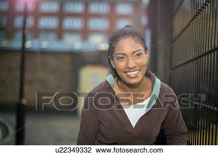 Stock Image - Young woman beside fence, smiling. Fotosearch