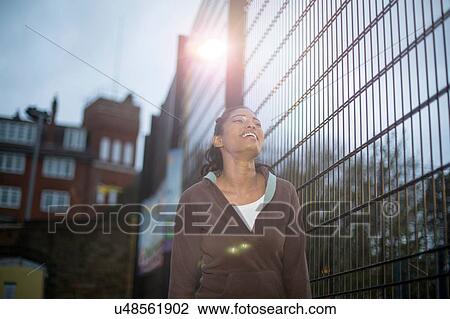 Stock Image - Young woman beside fence, smiling. Fotosearch