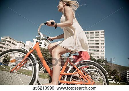 Stock Photograph - Young woman cycling past buildings, Cape Town, South Africa. Fotosearch