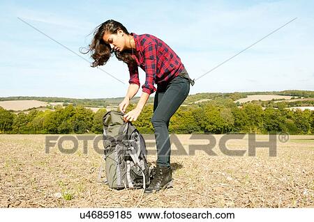 Stock Photography - Young woman fastening rucksack in field landscape, Great Missenden, Buckinghamshire, U. K. Fotosearch