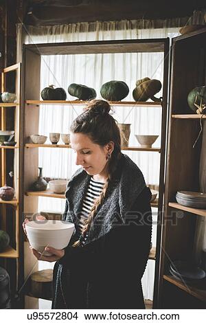 Young woman holding ceramic dish in front of shelves displaying clay pots and pumpkins View Large Photo Image Picture - Young woman holding ceramic dish in front of shelves displaying clay pots and pumpkins. Fotosearch