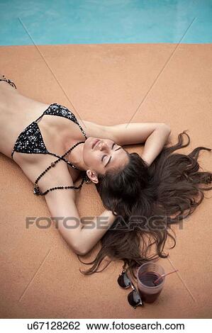 Stock Image - Young woman in bikini relaxing beside swimming pool. Fotosearch