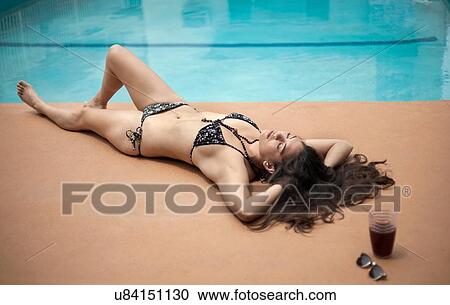 Stock Image - Young woman in bikini relaxing beside swimming pool. Fotosearch