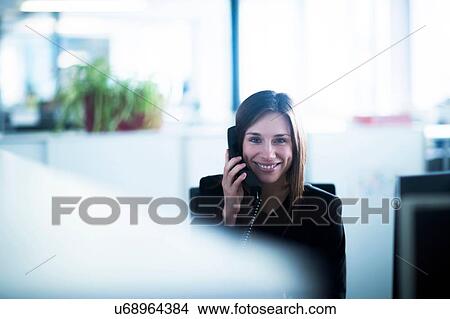 Young woman in office using telephone looking at camera smiling View Large Photo Image Picture - Young woman in office using telephone looking at camera smiling. Fotosearch