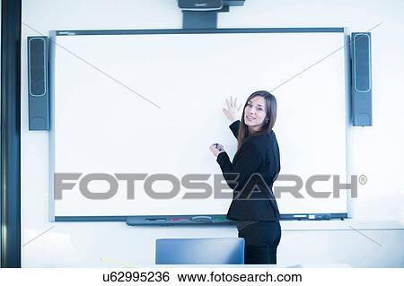 Young woman in office using whiteboard, looking over shoulder at camera smiling View Large Photo Image Stock Photograph - Young woman in office using whiteboard, looking over shoulder at camera smiling. Fotosearch