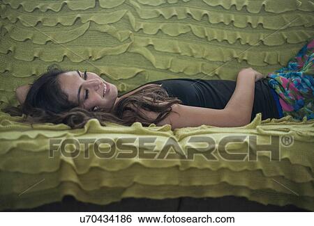 Young woman lying on back on ruffled blanket on sofa, looking away smiling View Large Photo Image Stock Photograph - Young woman lying on back on ruffled blanket on sofa, looking away smiling. Fotosearch