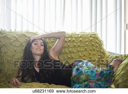 Young woman lying on side on ruffled blanket on sofa, hand on forehead looking at camera smiling View Large Photo Image Stock Photo - Young woman lying on side on ruffled blanket on sofa, hand on forehead looking at camera smiling. Fotosearch