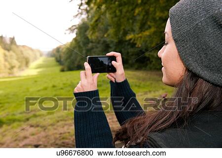 Stock Image - Young woman photographing field on smartphone. Fotosearch