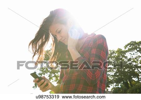 Young woman reading smartphone texts against sunlit sky View Large Photo Image Stock Photo - Young woman reading smartphone texts against sunlit sky. Fotosearch