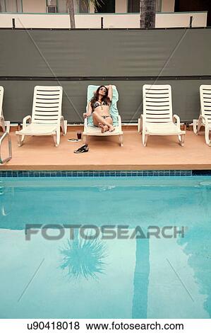 Stock Photo - Young woman relaxing on deck chair beside swimming pool. Fotosearch