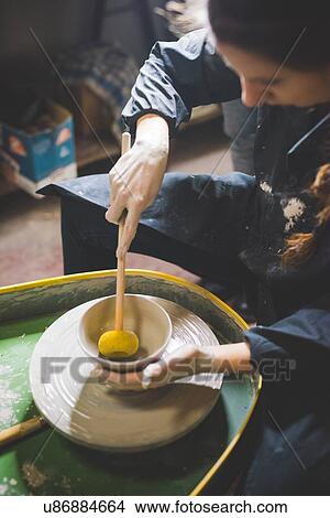 Young woman sitting at pottery wheel forming clay pot with diddler View Large Photo Image Picture - Young woman sitting at pottery wheel forming clay pot with diddler. Fotosearch