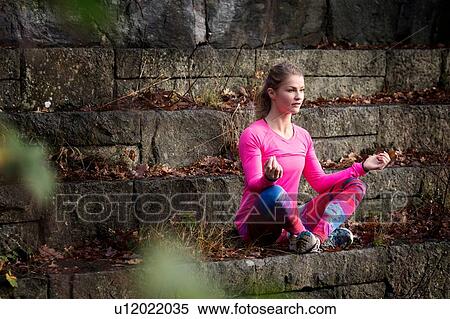 Stock Photography - Young woman sitting cross legged on stone steps meditating looking away. Fotosearch