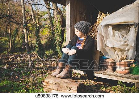 Stock Photo - Young woman sitting in storage shed wearing knit hat looking away. Fotosearch