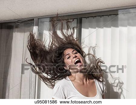 Stock Photograph - Young woman throwing hair back, in front of sliding doors. Fotosearch