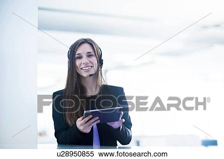 Young woman wearing telephone headset holding digital tablet looking at camera smiling View Large Photo Image Stock Photography - Young woman wearing telephone headset holding digital tablet looking at camera smiling. Fotosearch