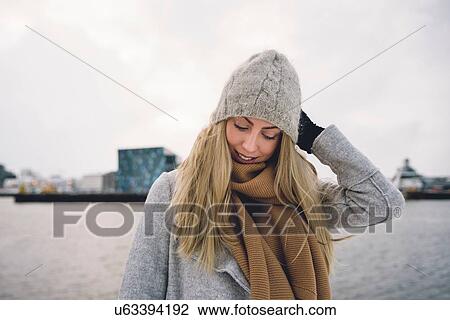 Young woman wearing woollen hat and scarf by water looking down smiling View Large Photo Image Stock Image - Young woman wearing woollen hat and scarf by water looking down smiling. Fotosearch