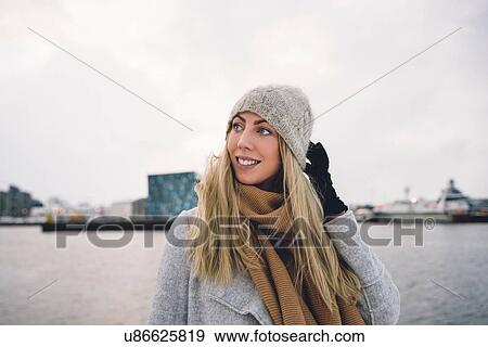 Young woman wearing woollen hat and scarf by water looking away smiling View Large Photo Image Stock Photo - Young woman wearing woollen hat and scarf by water looking away smiling. Fotosearch