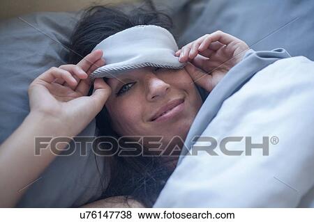 Stock Photo - Young woman with eye mask in bed. Fotosearch