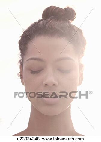 Stock Photo - Young woman with hair bun, eyes closed. Fotosearch