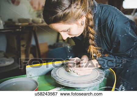 Stock Photo - Young woman with plaited hair using pottery wheel. Fotosearch