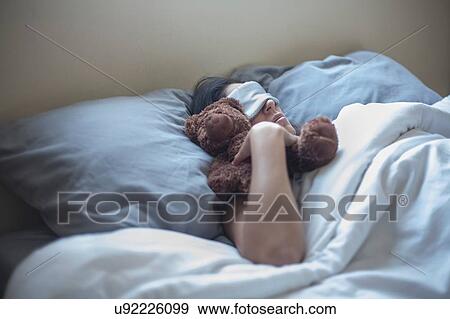 Stock Photo - Young woman with teddy bear, sleeping in bed. Fotosearch