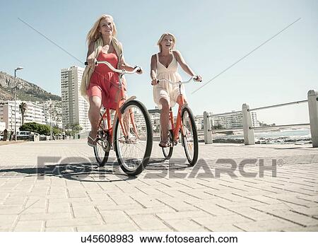 Stock Image - Young women cycling on seafront, Cape Town, South Africa. Fotosearch