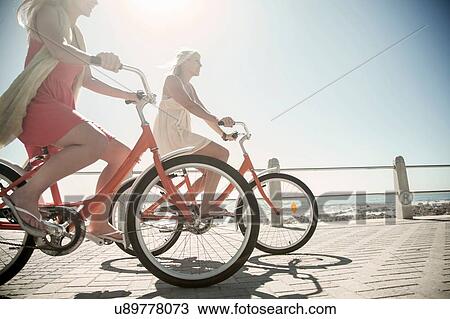 Stock Image - Young women cycling on seafront, Cape Town, South Africa. Fotosearch