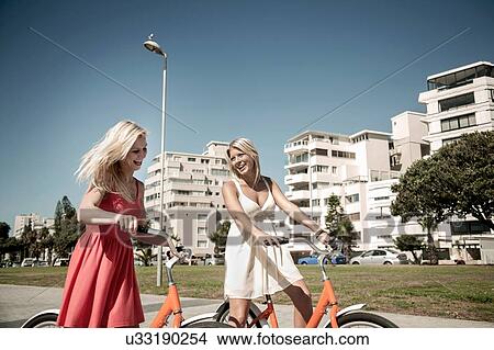 Picture - Young women walking with bicycle past buildings, Cape Town, South Africa. Fotosearch