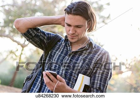 Stock Image - "Angled view of young man, hand to head, looking down at smartphone". Fotosearch