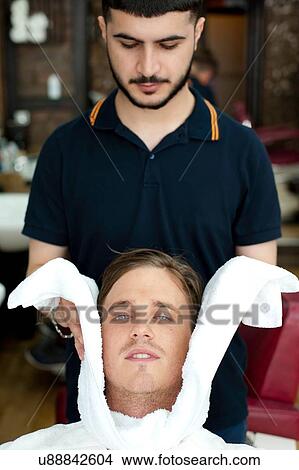 Barber wrapping young mans face in fresh towel, looking down View Large Photo Image Picture - Barber wrapping young mans face in fresh towel, looking down. Fotosearch