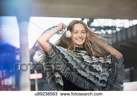 Stock Image - Beautiful mid adult woman wearing poncho and headphones dancing in city. Fotosearch