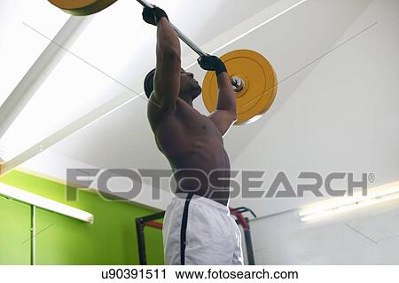 Stock Image - Bodybuilder lifting barbell in gym. Fotosearch