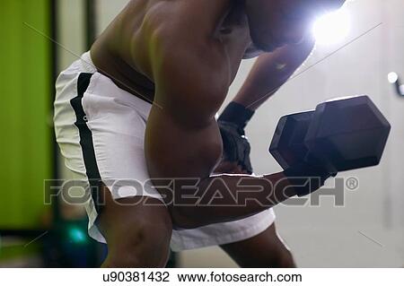 Stock Image - Bodybuilder lifting dumbbell in gym. Fotosearch