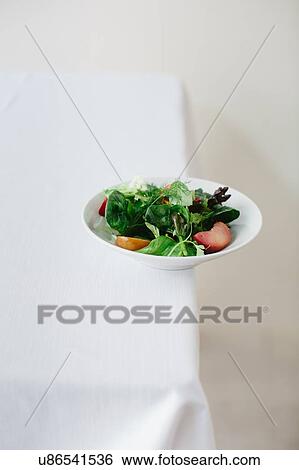 Stock Photograph - Bowl of green salad, apples and dill balanced on edge of table. Fotosearch