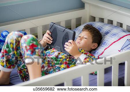 Boy in bed using a digital tablet View Large Photo Image Stock Image - Boy in bed using a digital tablet. Fotosearch