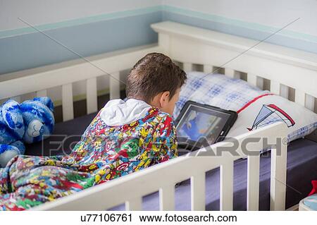 Stock Image - Boy in bed using a digital tablet. Fotosearch
