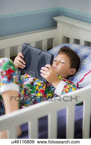 Boy in bed using a digital tablet View Large Photo Image Stock Photo - Boy in bed using a digital tablet. Fotosearch