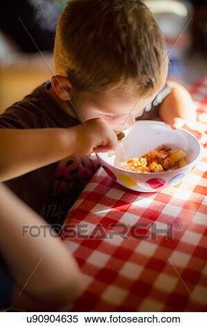 Boy sitting at table eating a meal View Large Photo Image Stock Photography - Boy sitting at table eating a meal. Fotosearch