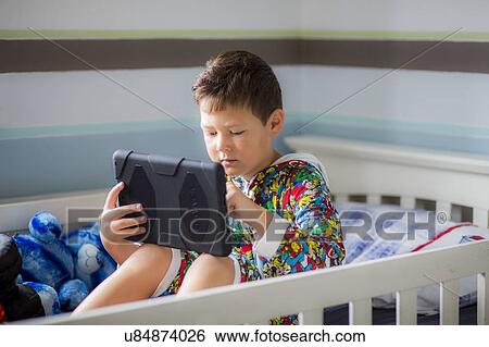 Boy sitting in bed using a digital tablet View Large Photo Image Stock Photograph - Boy sitting in bed using a digital tablet. Fotosearch