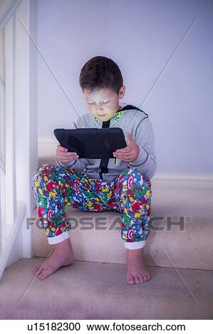 Boy sitting on a step using a tablet View Large Photo Image Stock Image - Boy sitting on a step using a tablet. Fotosearch